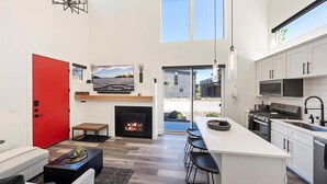 Eine moderne Küche mit Kochinsel, Kamin und großem Fenster mit Blick auf eine Terrasse.