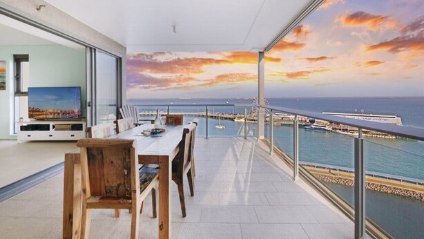 A modern living room with a large glass door leading to a balcony overlooking a marina and ocean. - ZEN POINT PENTHOUSE - 3 BR Waterfront (Darwin)