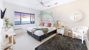A modern bedroom with a bed, bedside tables, a chair, a large window with a view, and a ceiling fan. - ZEN POINT PENTHOUSE - 3 BR Waterfront (Darwin)