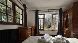 Een hotelkamer met een groot bed, een houten dressoir, een bureau en uitzicht op groen door de ramen.