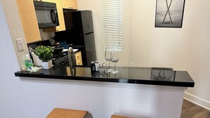 A compact kitchen with a black countertop, two wooden stools, and a microwave above the sink. - 1 bd Apt in Marina Del Rey - Venice. Resort style complex with premium amenities (Marina del Rey)