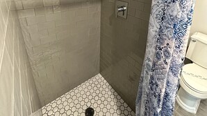 A shower area with hexagonal patterned tiles, a showerhead, and a towel rack with toiletries.