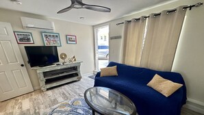 A living room with a blue sofa, a glass coffee table, a TV on a wooden stand, and a patterned rug.