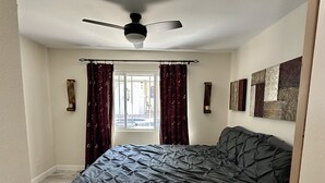 A bedroom with a large bed, a ceiling fan, and a window with curtains.