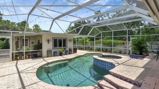 A covered outdoor swimming pool with a curved design, surrounded by potted plants and a patio area.