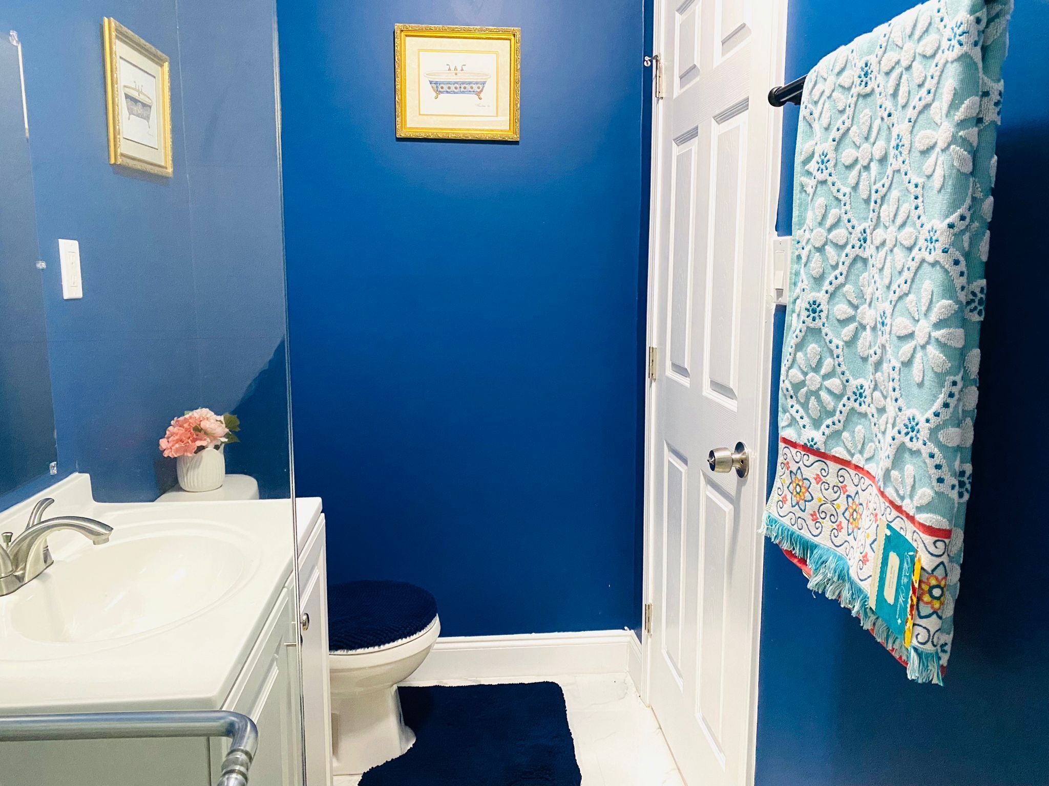 Een badkamer met een blauwe wand, een witte wastafel, een toilet en een deur met een handdoek met een patroon.