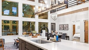 A modern kitchen with a large island, multiple windows, and a dining area with a staircase. - ✨Hampton's Hideaway: Luxury cabin with 🎲 Games, 🪁 Playground, and 💦 Hot Tub✨ (Broken Bow)