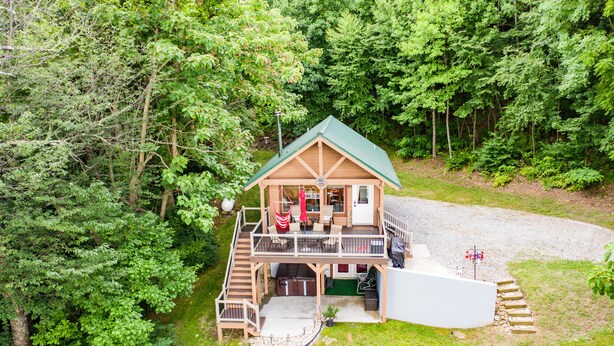 A two-story log cabin with a green roof, a deck, and a covered outdoor seating area. - RELAX - HOT TUB & GORGEOUS MOUNTAIN VIEWS                                    (Amherst)