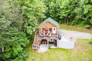 A two-story log cabin with a green roof, a deck, and a covered outdoor seating area. - RELAX - HOT TUB & GORGEOUS MOUNTAIN VIEWS (Amherst)