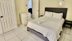 A bedroom with a bed, a dresser, a door, and a wall decoration. - Stylish modern apt beach view (Belmont)