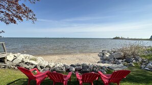 A lakeside view with a row of red Adirondack chairs facing the water, surrounded by rocks and a wooden deck. - Waterfront home w/beach, pool, and tennis. 5 min to Blue Mountain.  (Collingwood)