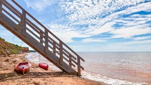 Ein Strand mit einer Holztreppe, die zum Wasser führt, Kajaks und einem klaren Himmel.