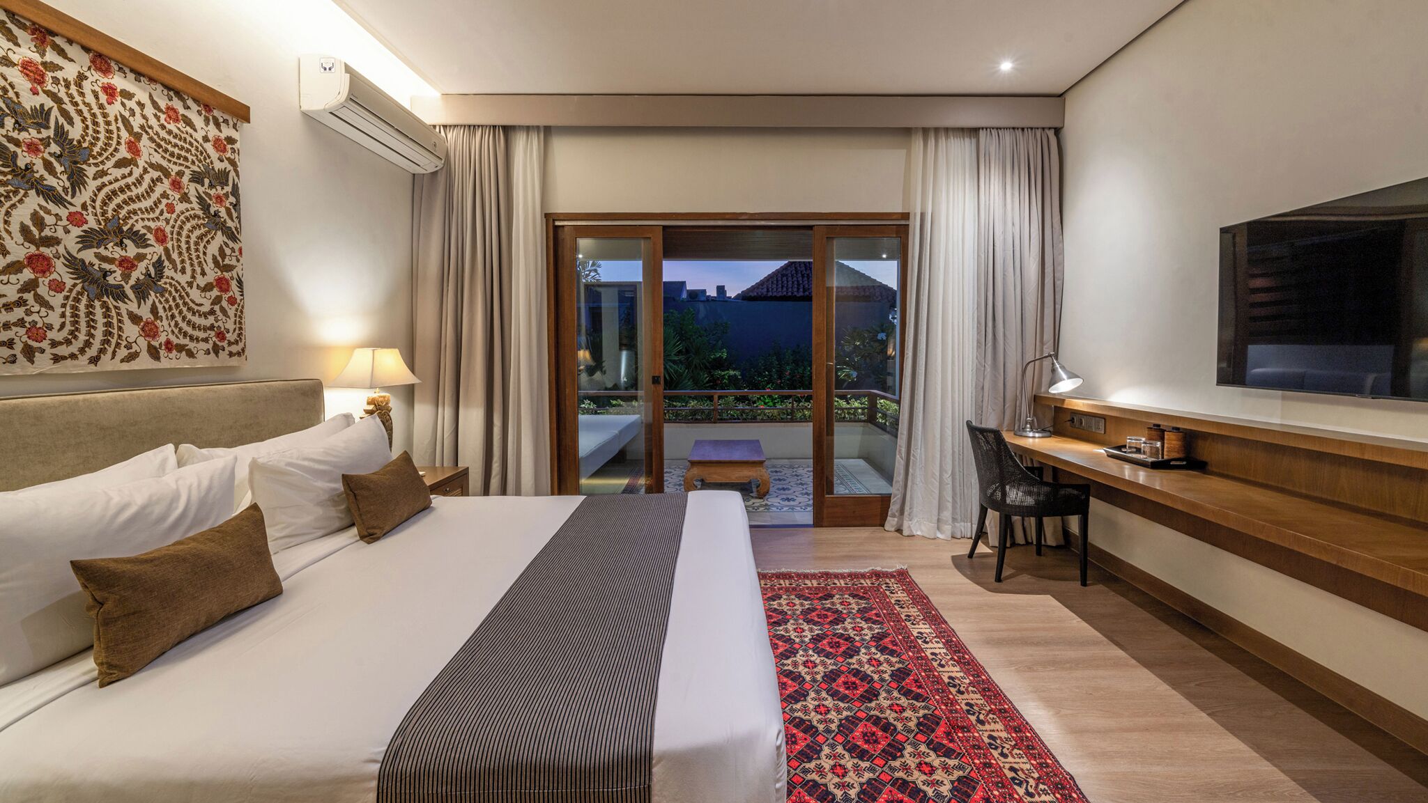 A hotel room with a bed, a desk, a TV, and a balcony with curtains.