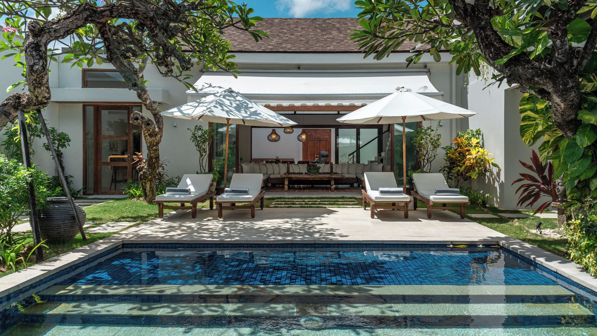 A pool area with lounge chairs, umbrellas, and a dining area with a sofa and table.