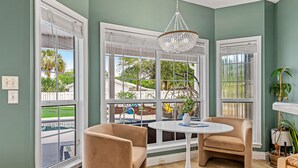 Una habitación con ventanas amplias, una mesa redonda, dos sillas y una lámpara colgante.