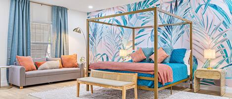 A bedroom with a four-poster bed, a grey sofa, and a white rug.
