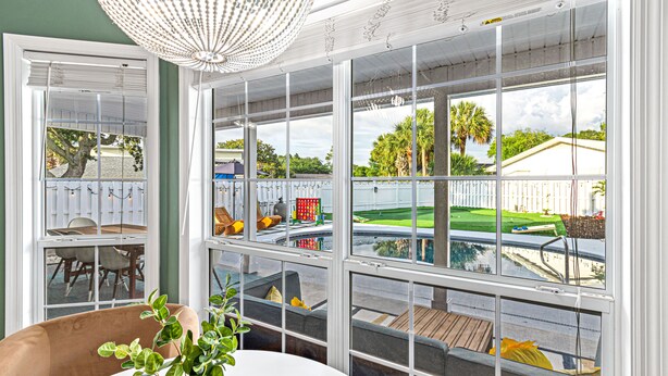 Una habitación con un amplio ventanal que da a un patio trasero con piscina, terraza de madera y cerca blanca.