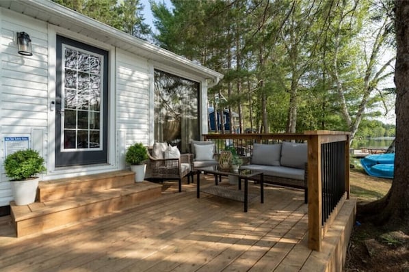 Relax on the deck with a sofa, coffee table, and chairs, surrounded by lush greenery and a shaded pergola.