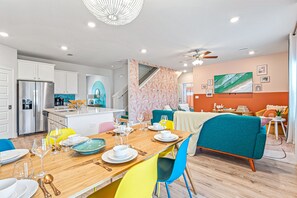 A modern kitchen with stainless steel appliances, a dining area with colorful chairs, and a living space with a teal sofa.