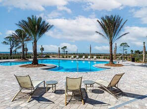 A pool area with lounge chairs and tables, surrounded by palm trees and a clear view of the ocean. - FullyLoaded5BR~Walk2Pool&Beach~Gameroom~Firepit~Sleeps16 (Port St. Joe)