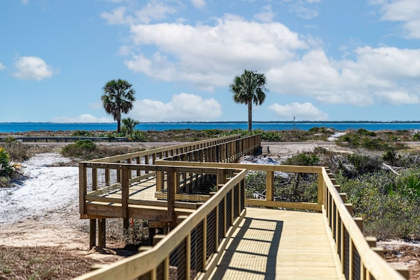 A wooden boardwalk leading to a beach with palm trees and a clear blue sky.