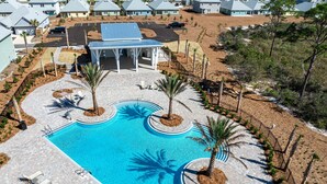 A large swimming pool with sun loungers and palm trees, surrounded by a paved area and a covered pavilion. - FullyLoaded5BR~Walk2Pool&Beach~Gameroom~Firepit~Sleeps16 (Port St. Joe)