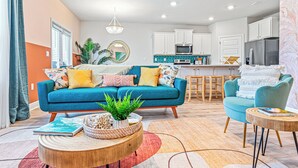 A modern living room with a blue sofa, a round coffee table, and a kitchen in the background. - FullyLoaded5BR~Walk2Pool&Beach~Gameroom~Firepit~Sleeps16 (Port St. Joe)