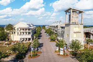 A coastal town with a prominent lighthouse, a main road lined with trees, and buildings with balconies. - FullyLoaded5BR~Walk2Pool&Beach~Gameroom~Firepit~Sleeps16 (Port St. Joe)