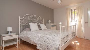 Une chambre à coucher avec un lit en métal blanc, une couvre-lit à motifs floraux, une table de chevet avec une lampe et une petite table de nuit.