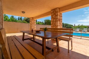 Une terrasse extérieure avec une table et des bancs en bois, des piliers en pierre et une vue sur une piscine.
