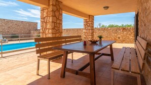 A patio with a pool, stone walls, wooden furniture, and a clear view of the pool.