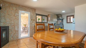 A dining area with a wooden table and chairs, a stone wall, and a kitchen in the background.