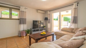A living room with a sofa, a coffee table with fruit, a TV, and a sliding glass door to the outside.