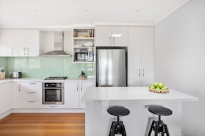 A modern kitchen with white cabinetry, a stainless steel refrigerator, a microwave, a gas stove, and a small island with stools.