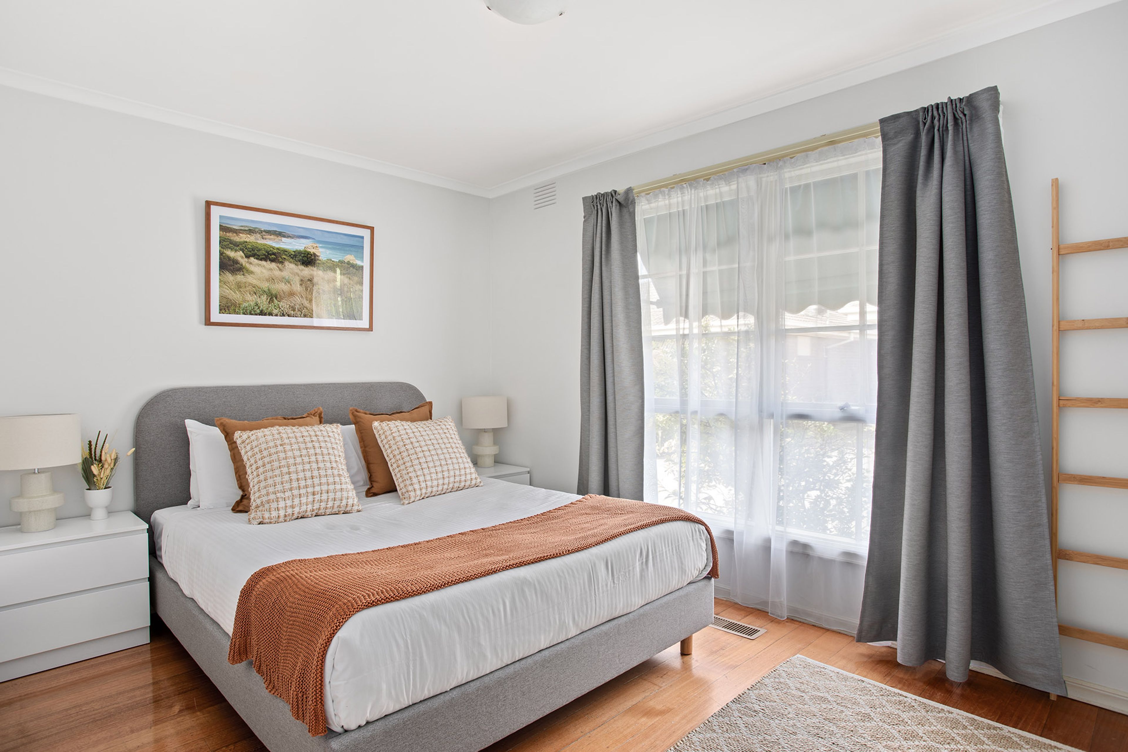 Une chambre à coucher avec un lit, des tables de chevet, une fenêtre avec des rideaux, une vue sur l’extérieur et un tableau encadré au mur.