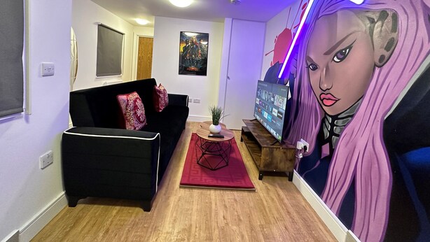 A living room with a black sofa, a red rug, a TV, and a wall mural.