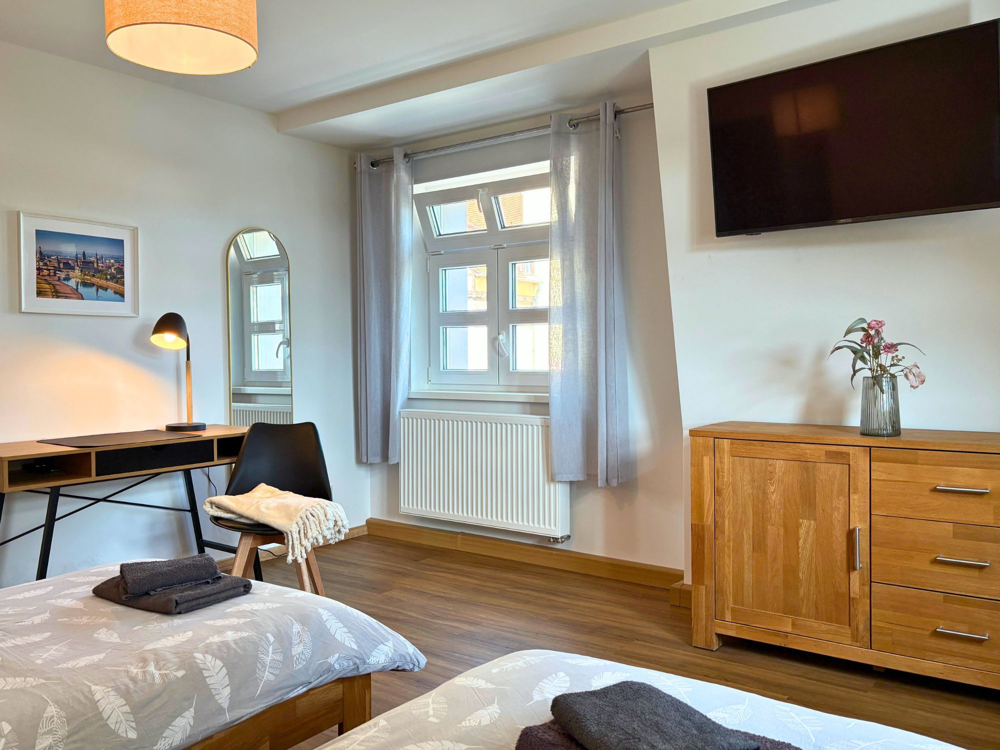 A hotel room with a bed, a desk, a chair, a radiator, a TV, and a cabinet.