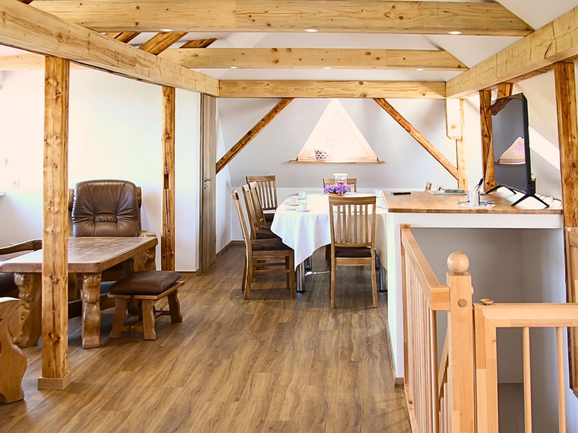 Una stanza con soffitto in legno, un tavolo da pranzo con sedie, una panca e una scrivania con un computer.
