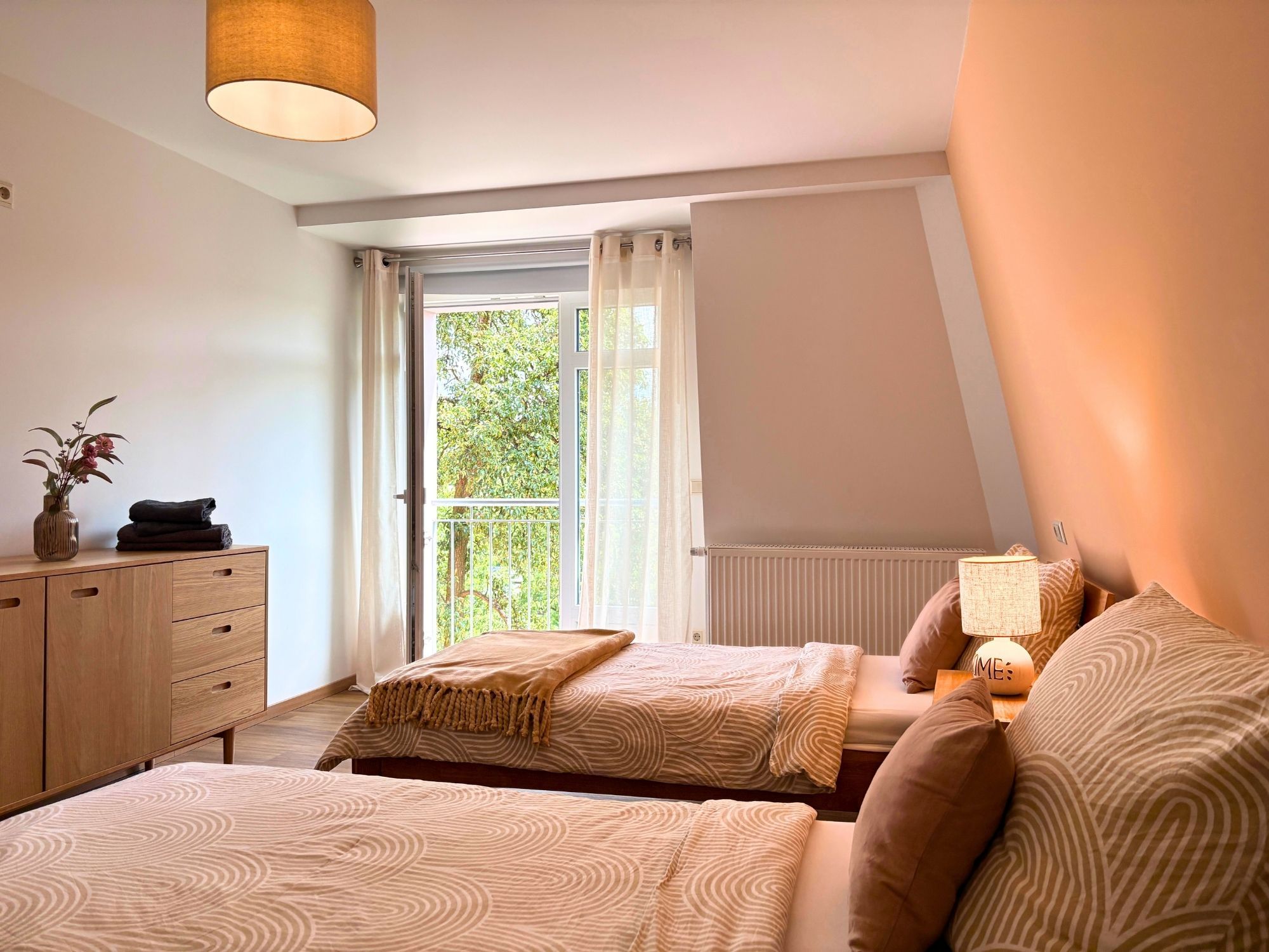 Een slaapkamer met twee bedden, een dressoir, een radiator en een raam met gordijnen.