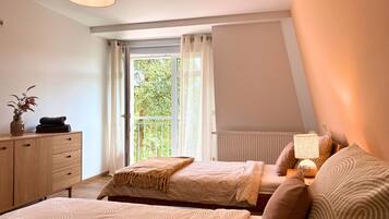 Een slaapkamer met twee bedden, een dressoir, een radiator en een raam met gordijnen.