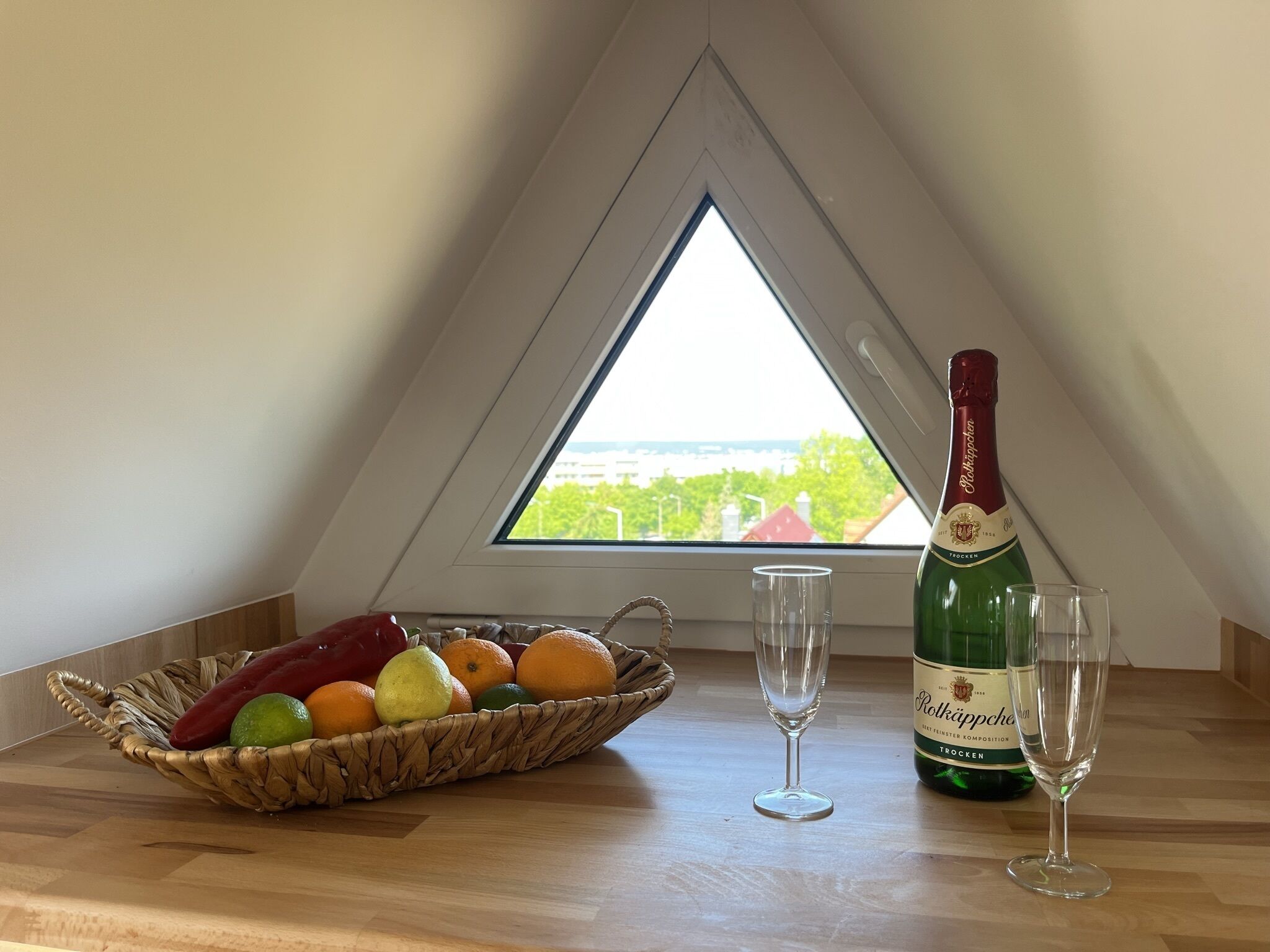 A room with a wooden table, a bottle of Poltkaffee, two glasses, and a fruit basket.