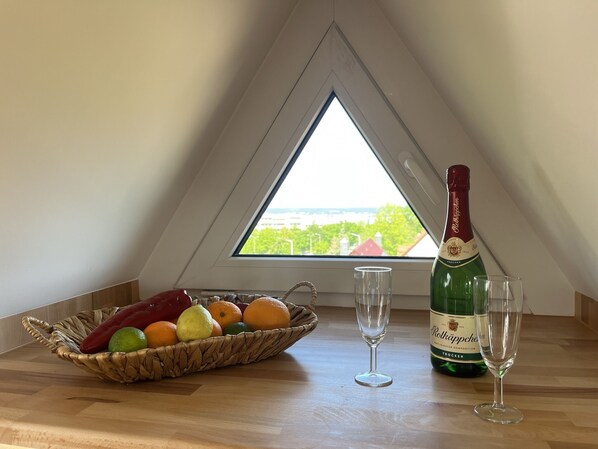 A room with a wooden table, a bottle of Poltkaffee, two glasses, and a fruit basket. - Maisonette Wohnung mit Dachterasse (Dresden)