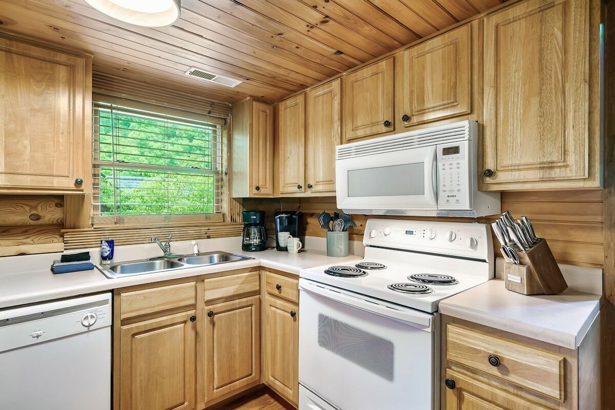 Une cuisine avec des meubles en bois, une cuisinière blanche, un four à micro-ondes et une fenêtre donnant sur un paysage verdoyant.