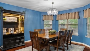 A dining area with a wooden table and chairs, a chandelier, and a coffee bar with a sign.