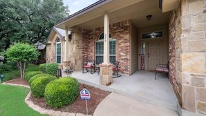 A two-story house with a brick exterior, a covered porch with outdoor seating, and a mailbox.