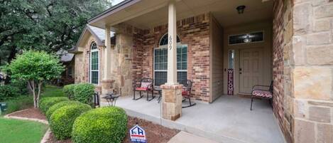 A two-story house with a brick exterior, a covered porch with outdoor seating, and a mailbox.