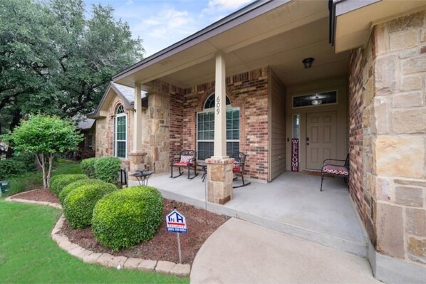 A two-story house with a brick exterior, a covered porch with outdoor seating, and a mailbox.