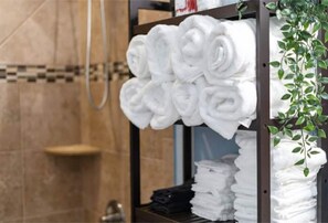 A bathroom with a towel rack holding neatly folded towels, a shower area, and a small plant.