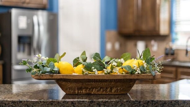 A kitchen counter with a wooden bowl containing lemons and herbs.