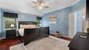 A bedroom with a dark wooden bed, a ceiling fan, a window with curtains, and a nightstand.